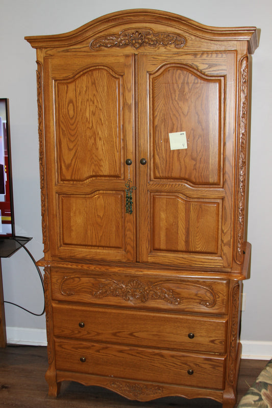 Front view of carved oak armoire wardrobe with paneled doors and drawers