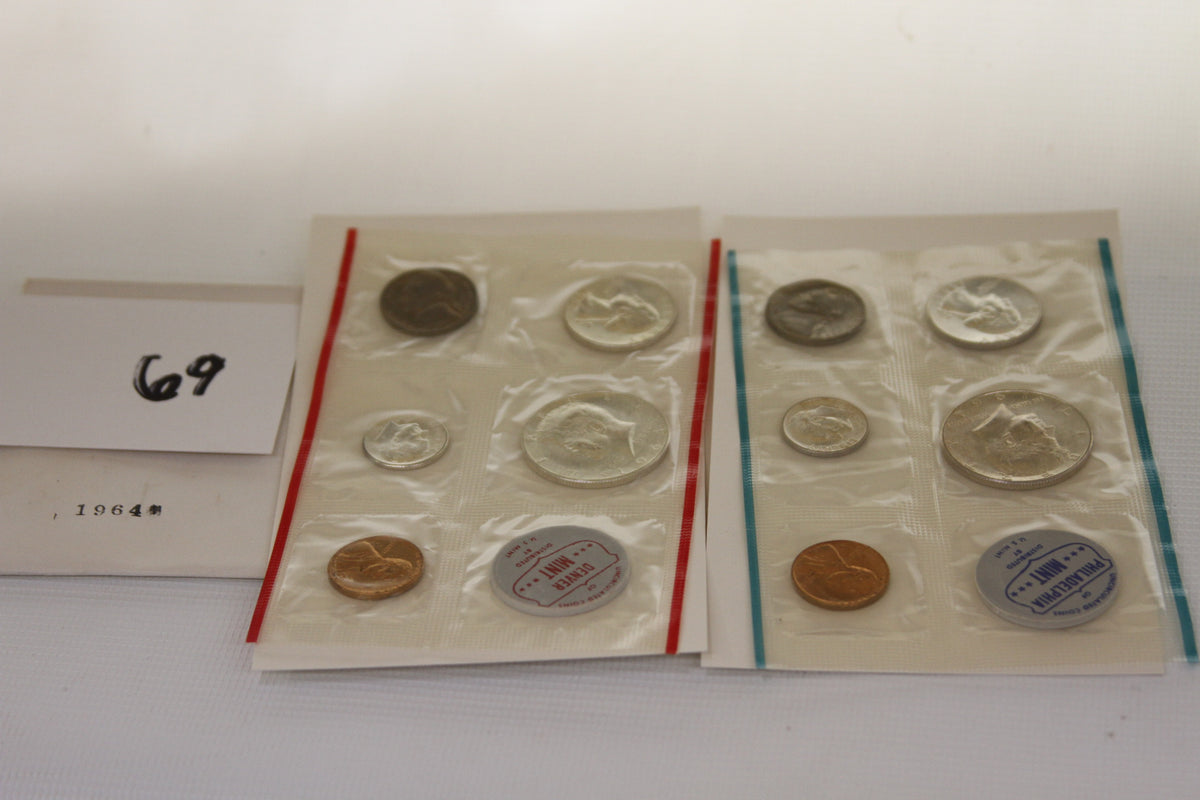 Two 1964 US Mint uncirculated coin sets in sealed packaging with visible coins and mint marks