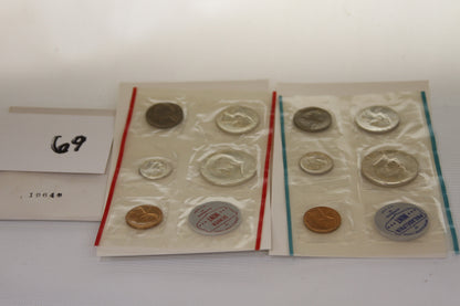 Two 1964 US Mint uncirculated coin sets in sealed packaging with visible coins and mint marks