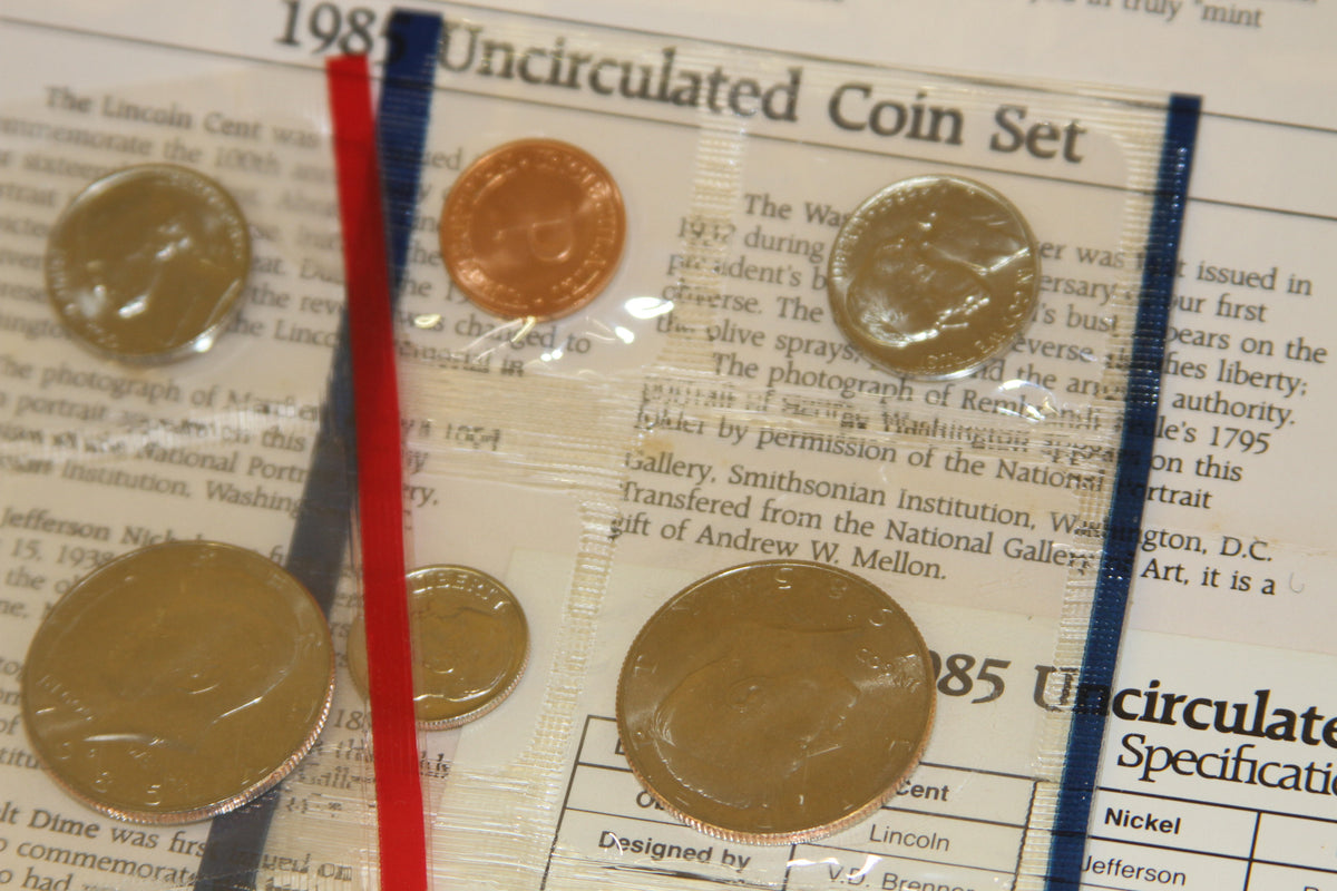 Multiple 1985 US coins in sealed packaging with specification sheets