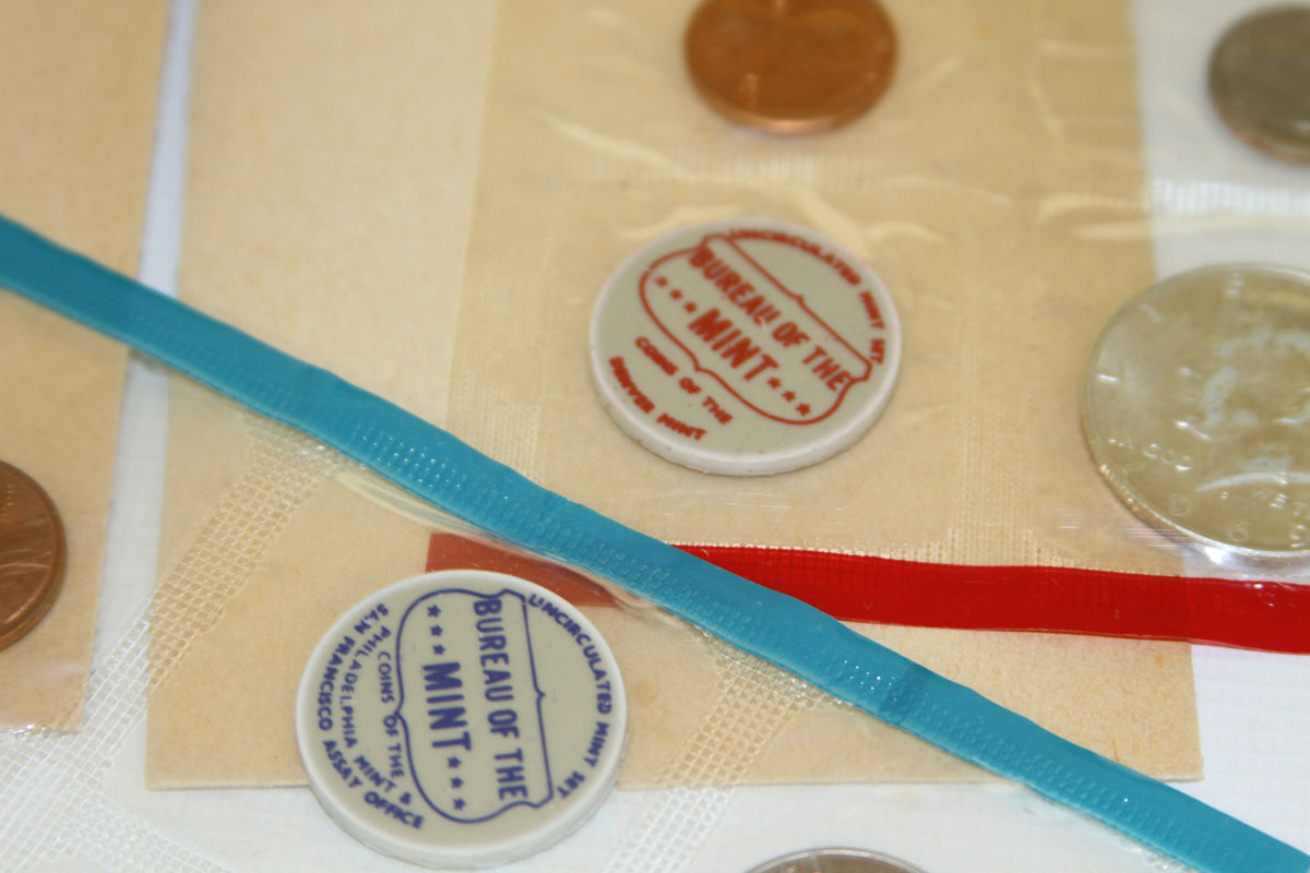 Blue and red Bureau of the Mint tokens beside uncirculated coins in packaging