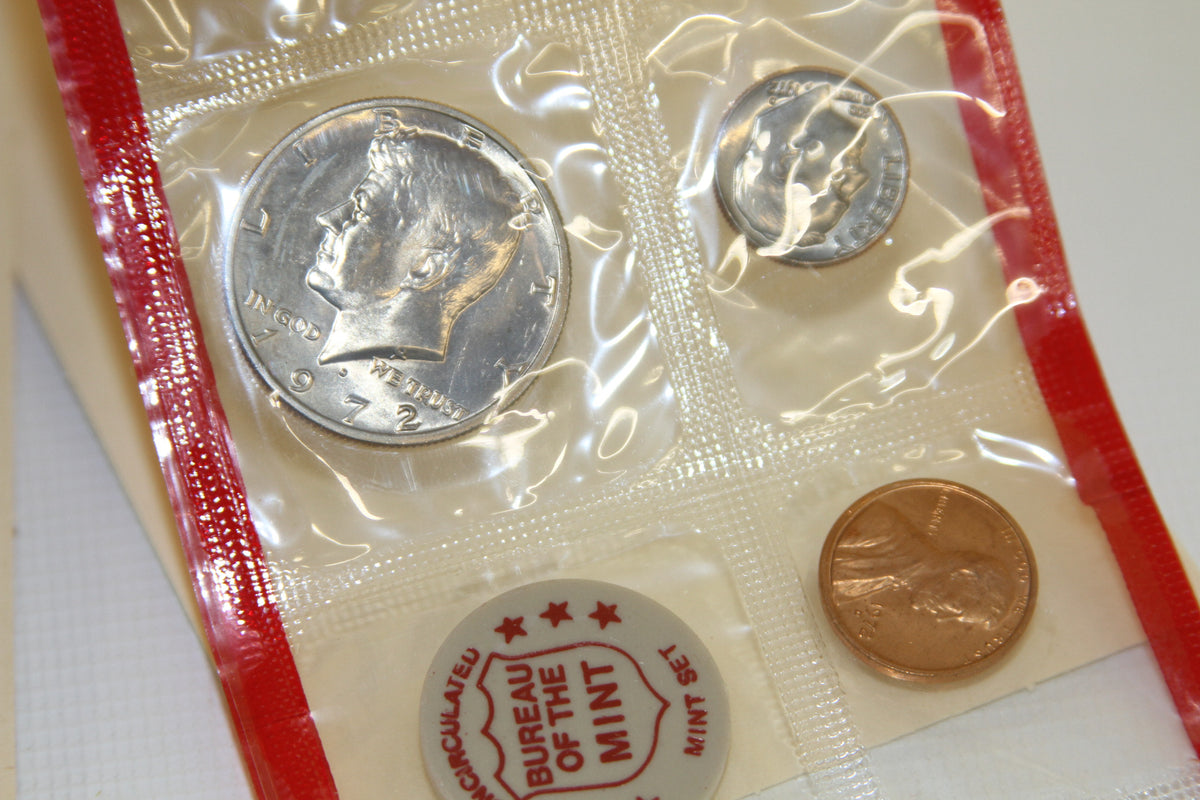 Detail of 1972 Kennedy half dollar, dime, penny, and mint token in red edged sleeve